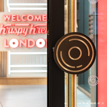 Krispy Kreme's illuminated entrance features a stylish door handle, welcoming visitors to the iconic London store.