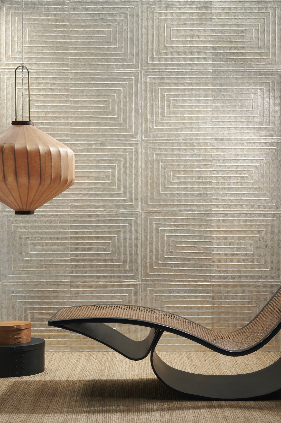 Elegant lounge chair positioned in front of textured wallcovering and warm pendant lamp, showcasing Arte's sophisticated Spring collections.