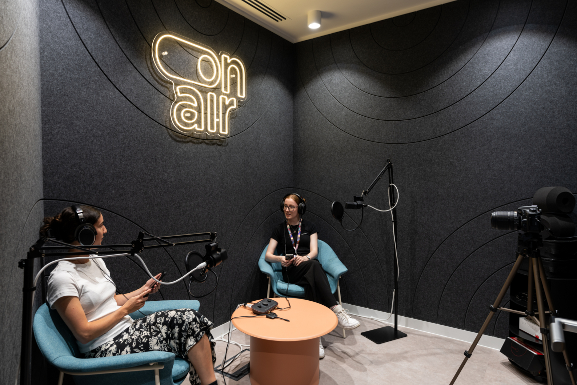 Vibrant coworking space featuring two women in a modern podcast studio with "on air" neon sign.