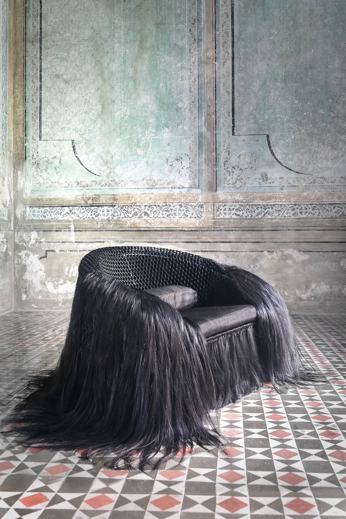 Artisan chair with long, flowing black fringe, set against a textured wall and patterned tile floor, highlighting Mexican craftsmanship.