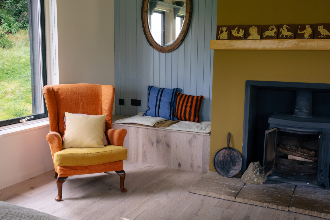 Cozy interior featuring Scandinavian design with orange armchair, textured cushions, and wood-burning stove in a retreat setting.