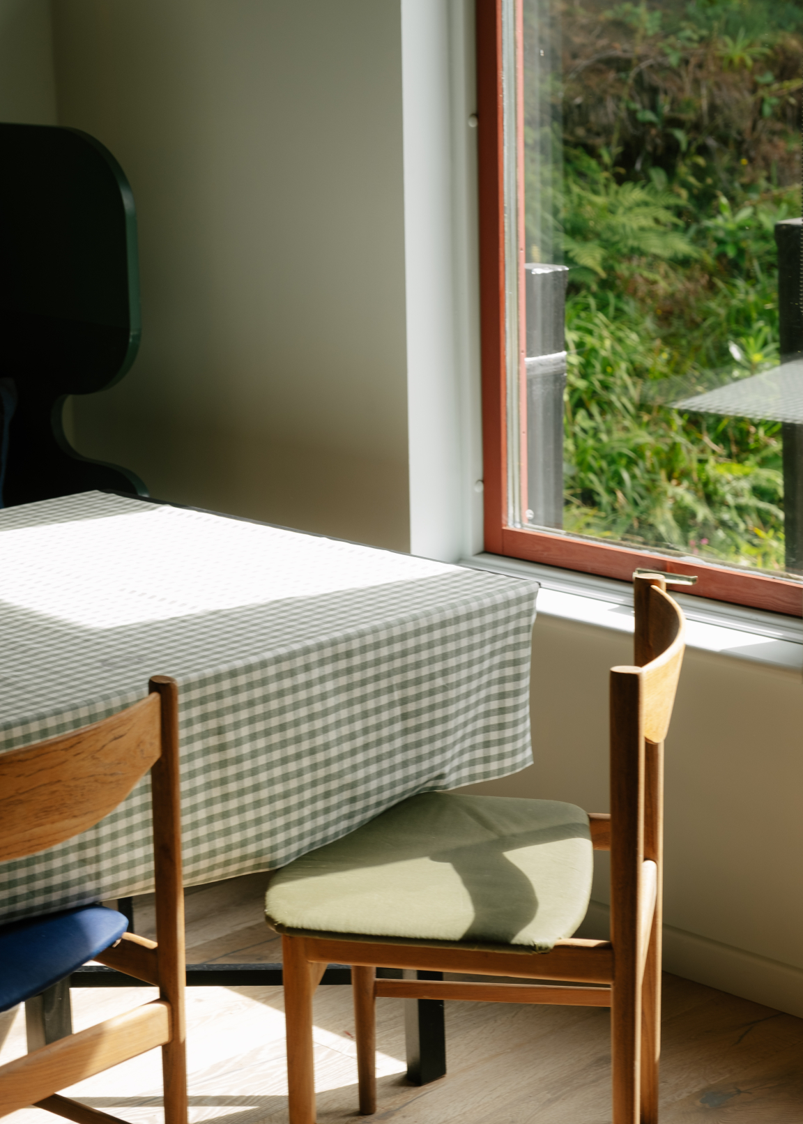 Bright dining area featuring a green checkered tablecloth, wooden chairs, and a view of lush greenery outside.