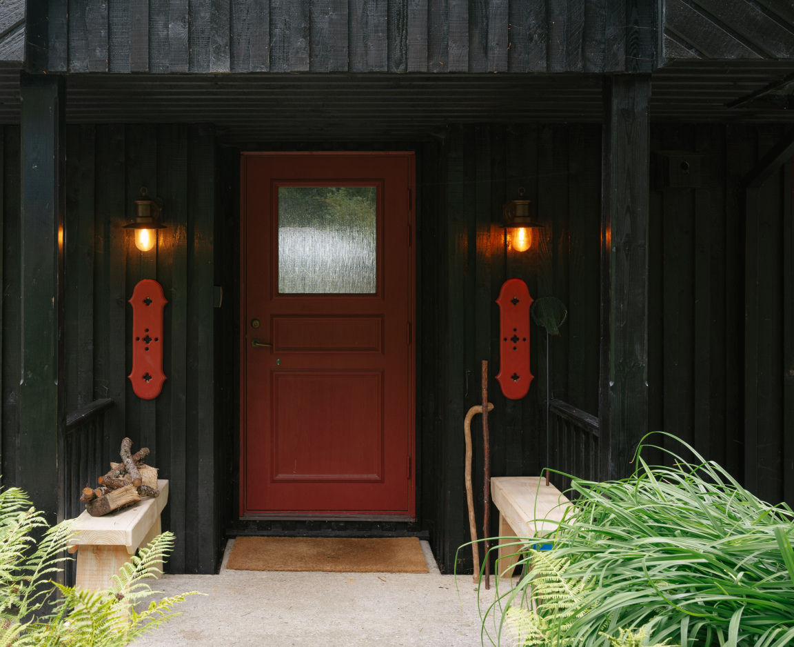 Black wooden exterior of a retreat featuring a striking red door, Scandinavian design elements, and lush greenery.