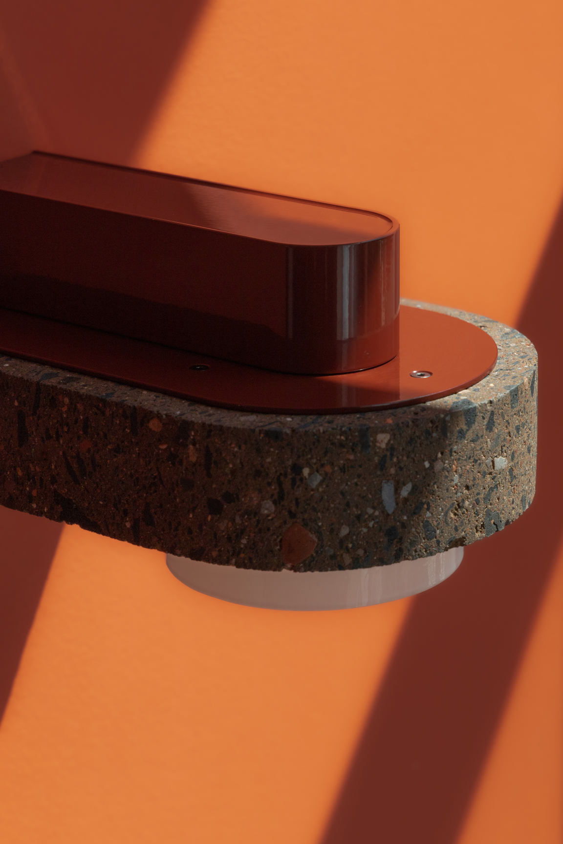 Modern lighting fixture featuring volcanic stone and sleek red design against a vibrant orange wall, showcasing davidpompa's innovative materiality.