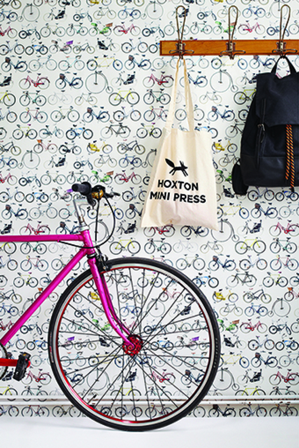 Bright pink bicycle leaning against a patterned wall featuring a collage of colorful bicycle illustrations.