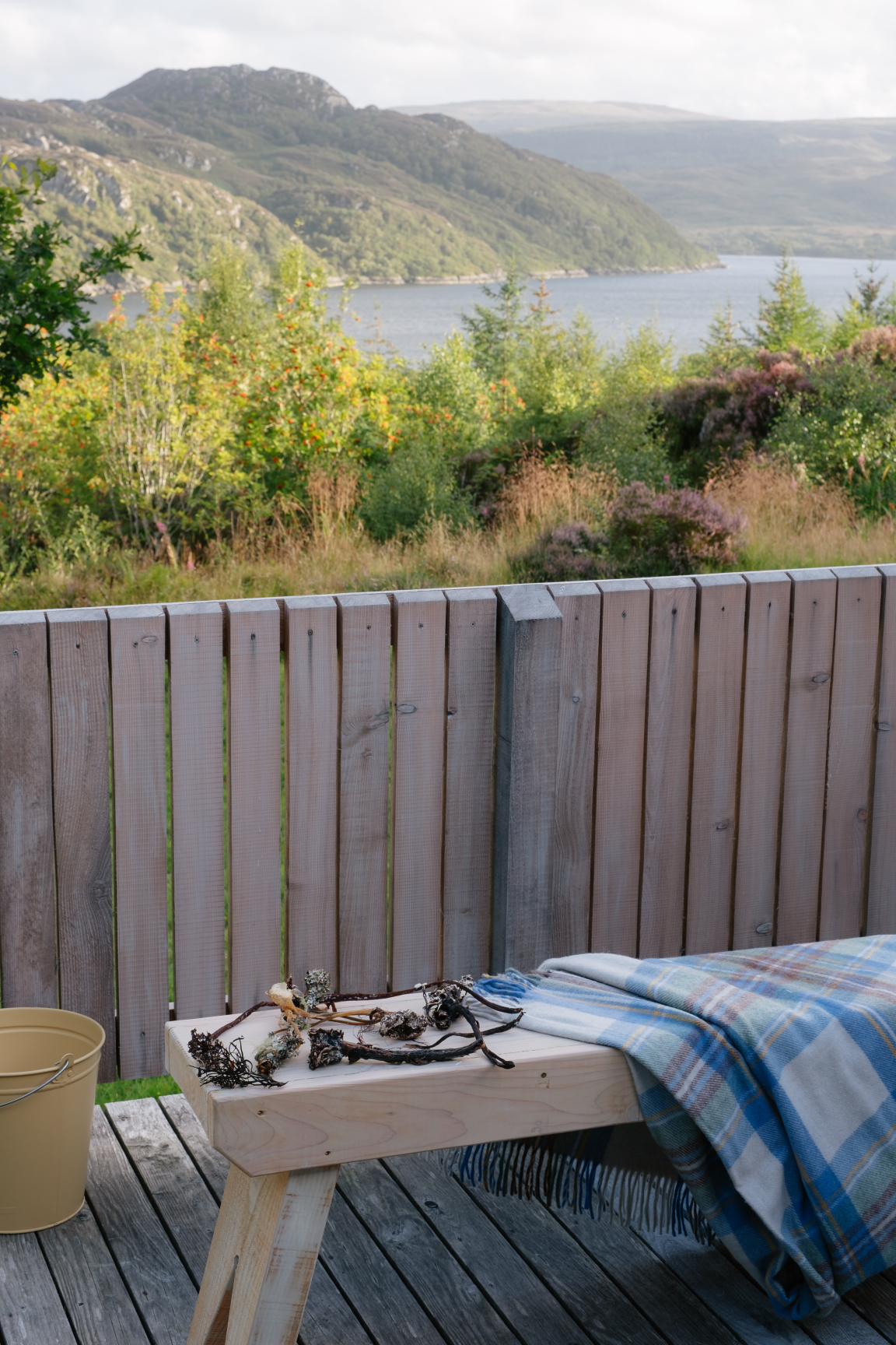 Serene outdoor retreat featuring Scandinavian timber decking, a cozy blanket, and natural decor overlooking a scenic landscape.