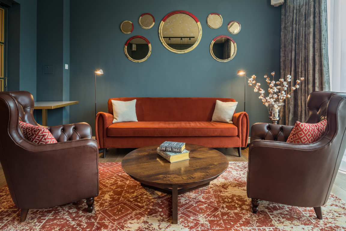 Stylish interior design featuring an orange sofa, brown leather armchairs, and decorative mirrors on a dark wall.