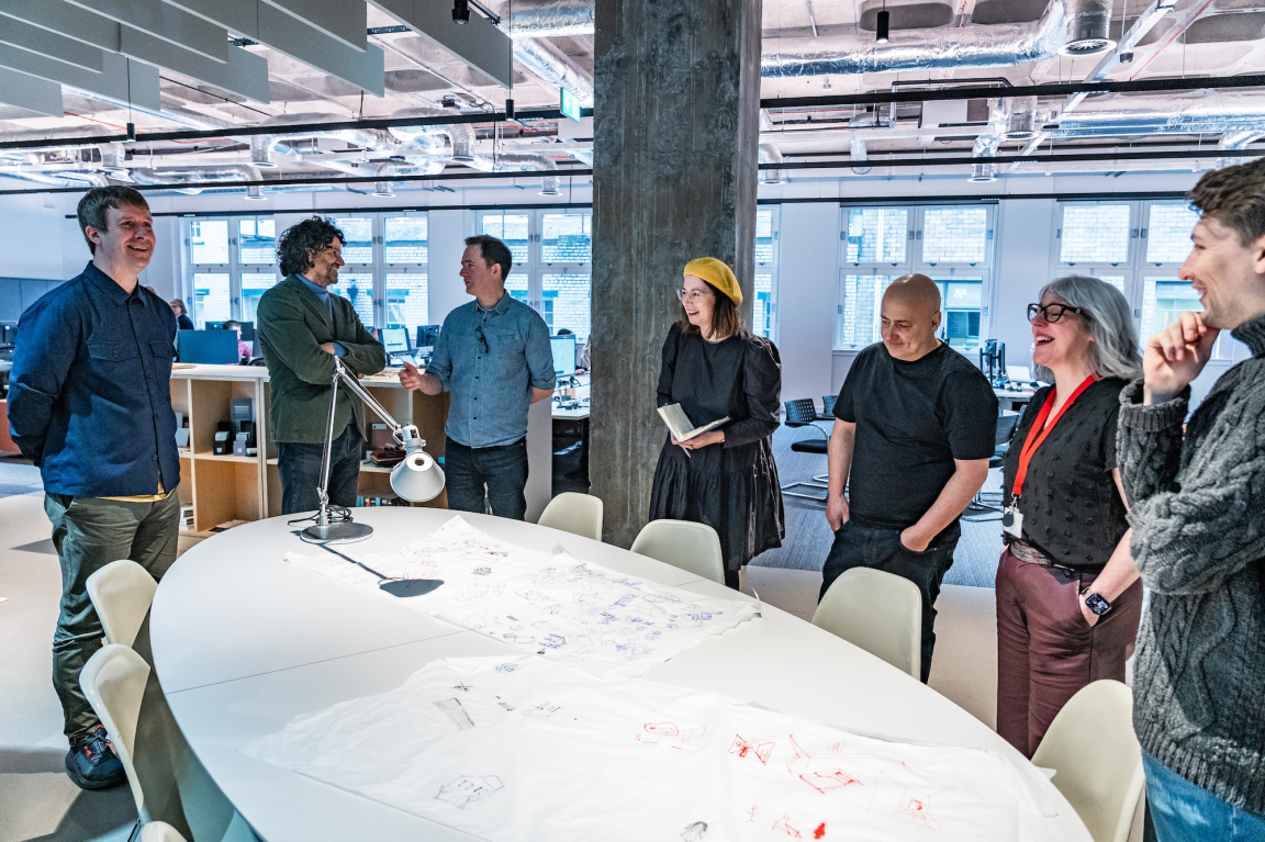 BDP Glasgow team collaborating in the new Grosvenor Building studio, discussing sketches and design ideas around a large table.