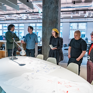 BDP Glasgow team collaborating in the new Grosvenor Building studio, discussing sketches and design ideas around a large table.