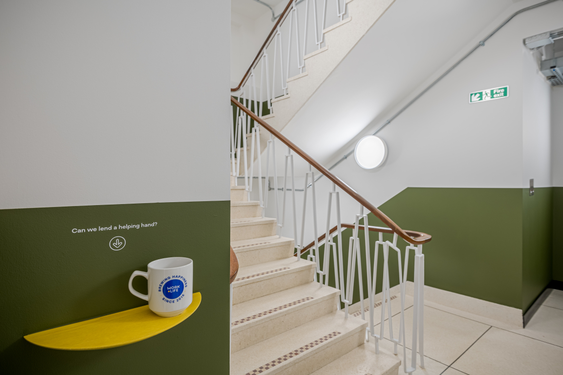 Modern staircase in the Typewriter building, featuring a yellow shelf with a coffee mug and motivational phrase.