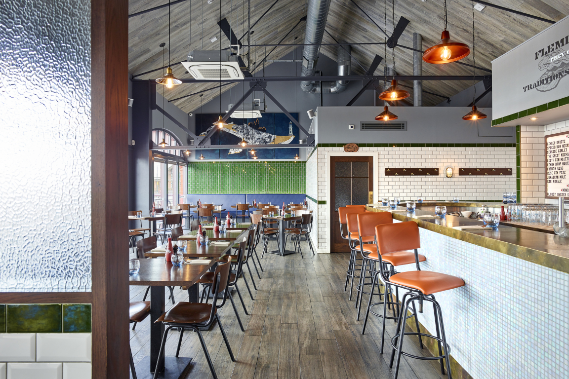 Modern restaurant interior featuring wooden flooring, green tile accents, and stylish bar seating in a vibrant Glasgow setting.