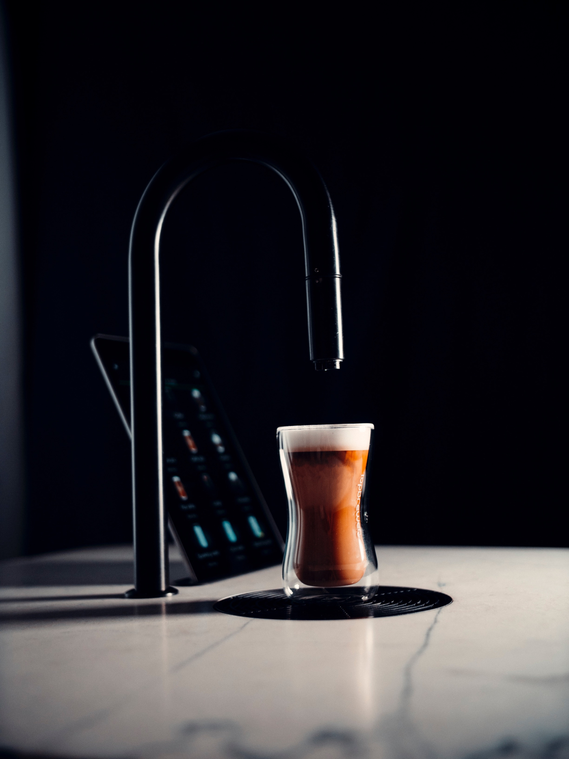 Sleek glass coffee cup sits on a marble countertop beside a modern touch-screen tablet, highlighting contemporary beverage experiences.