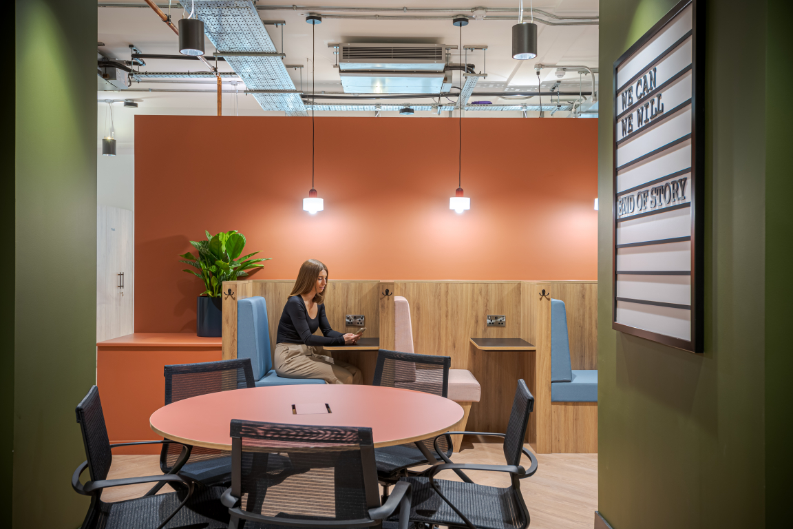 Modern co-working space featuring a stylish seating area with a woman using her phone and vibrant decor.