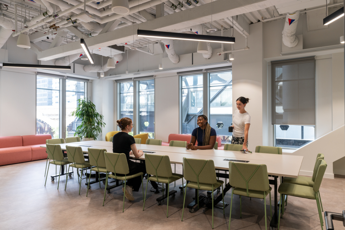 Modern coworking space showcasing vibrant furniture and diverse professionals collaborating at a long table with large windows.