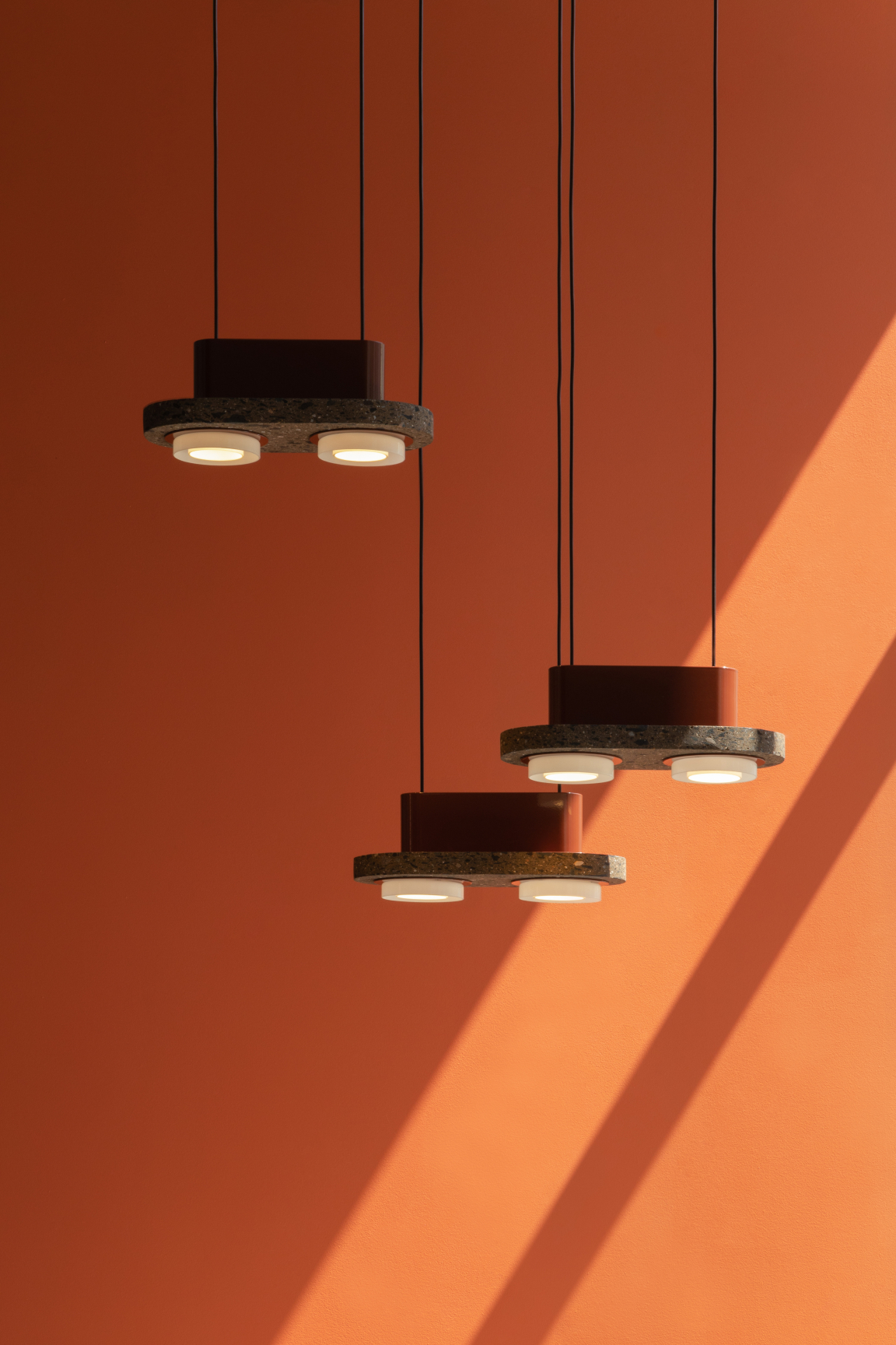 Volcanic material pendant lights by davidpompa cast soft illumination against a vibrant orange wall.