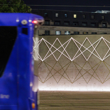 Manchester's Piccadilly Gardens Pavilion illuminated at night, featuring geometric light patterns on a concrete wall.