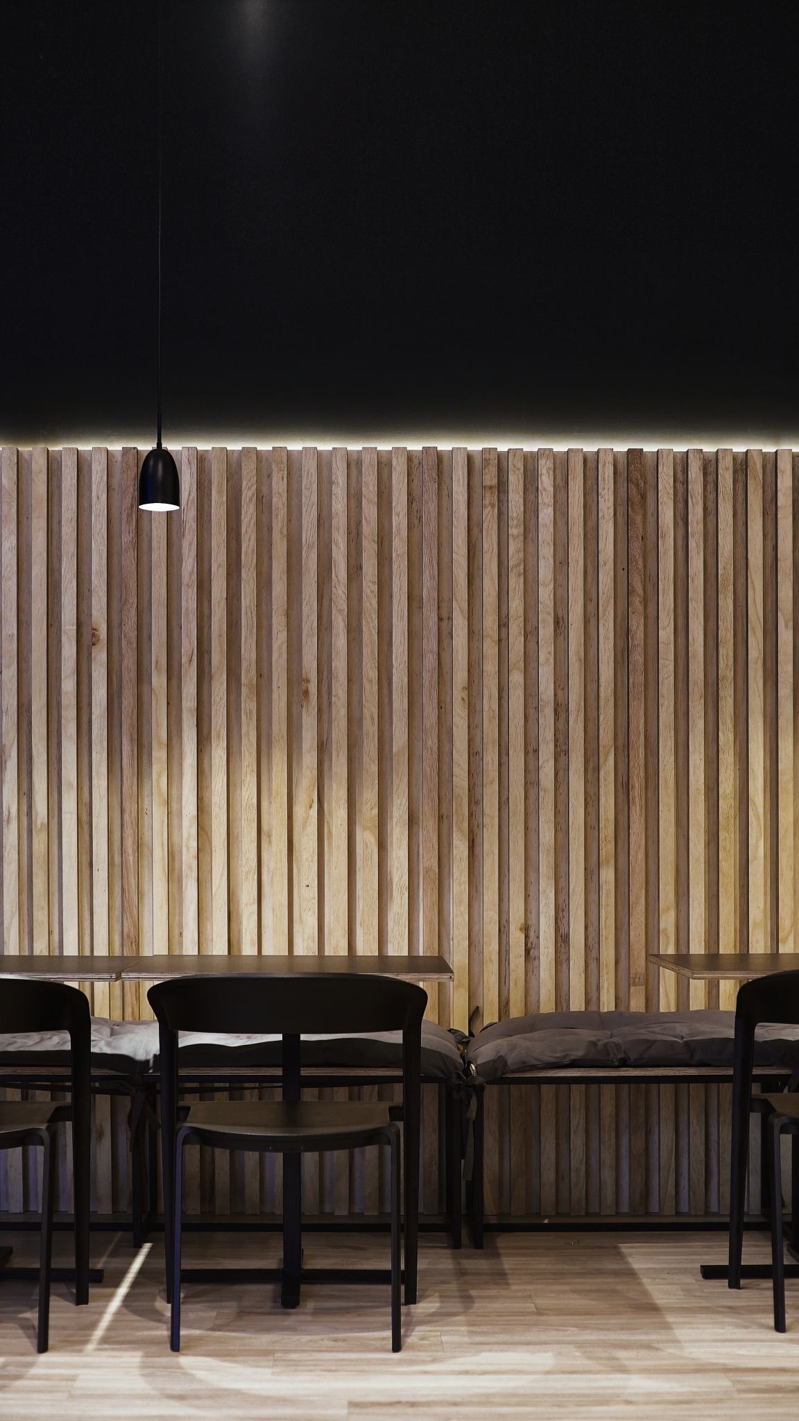 Intimate interior of Maru Asian Cuisine with wooden slat walls and modern black furniture, designed by Solo Arquitetos.