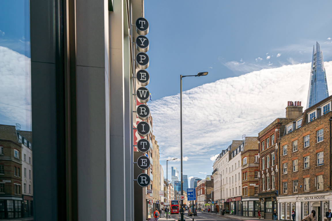 Co-working space Typewriter building sign with urban street view and modern architecture under a bright sky.