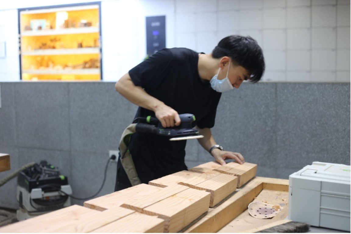 Zhekai Zhang using woodworking tools to shape sustainable materials in a design studio, highlighting innovative craft methods.