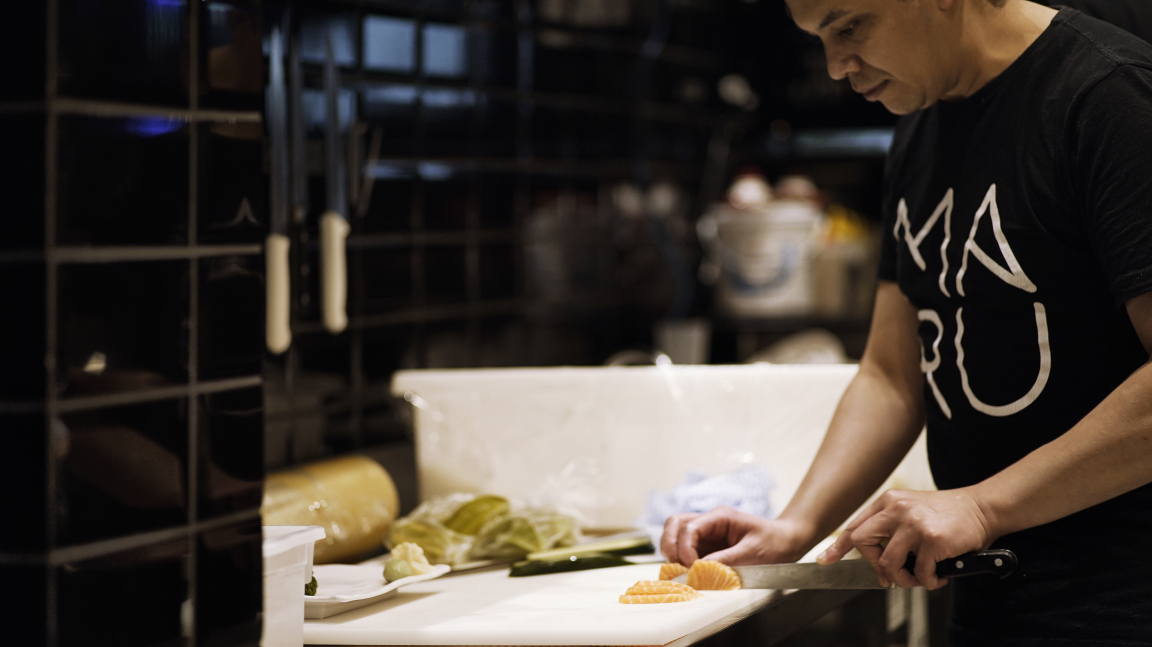 Chef preparing fresh ingredients in the intimate kitchen of Maru Asian Cuisine, showcasing a modern interior design.