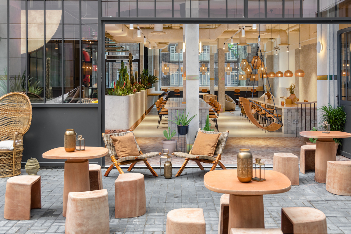 Welcoming outdoor seating area with modern furniture, greenery, and a view of the sustainable hotel design interior in Bermondsey.