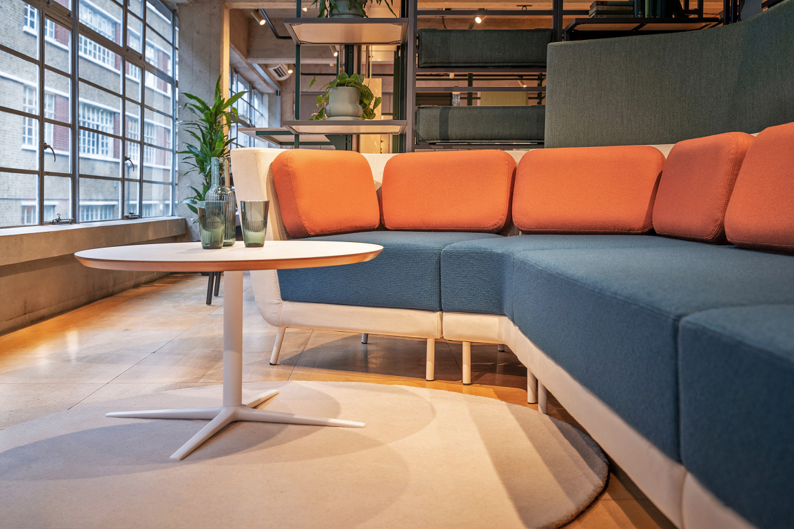 Stylish seating area featuring a modern couch with colorful cushions and a minimalist round table, ideal for Studio collaboration.