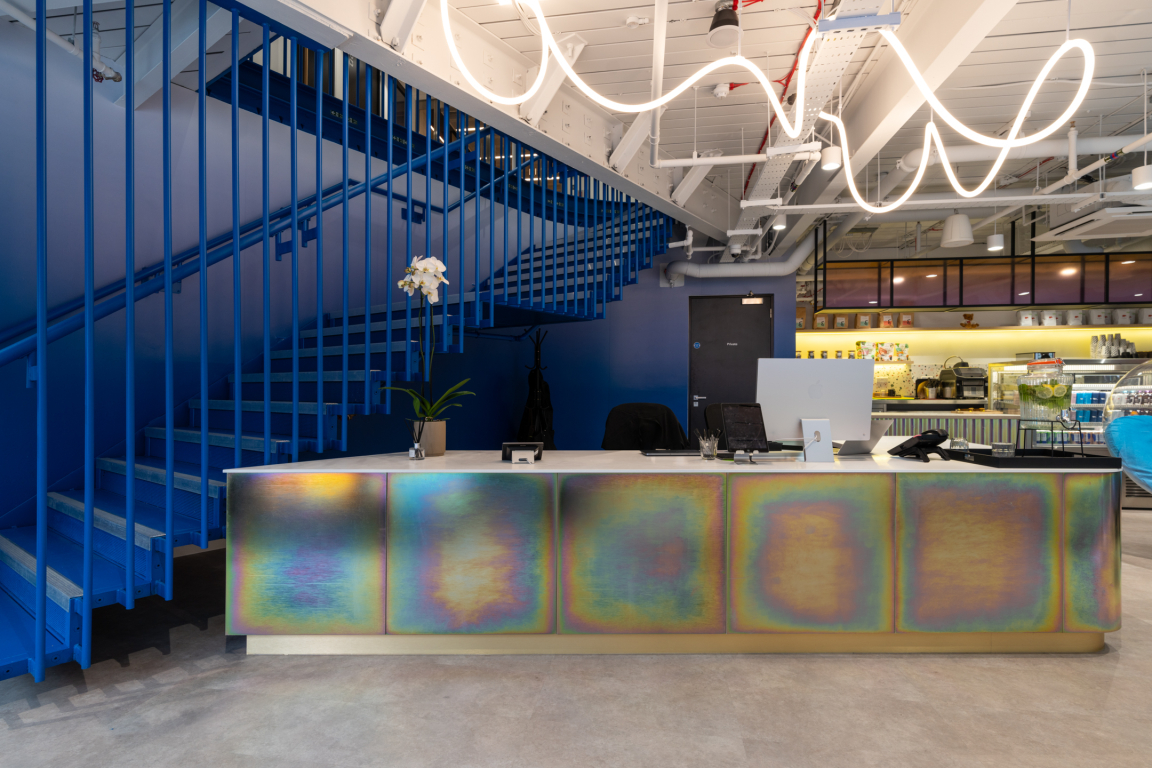 Vibrant reception area featuring multicolored desk, blue staircase, and modern lighting in Huckletree coworking space.