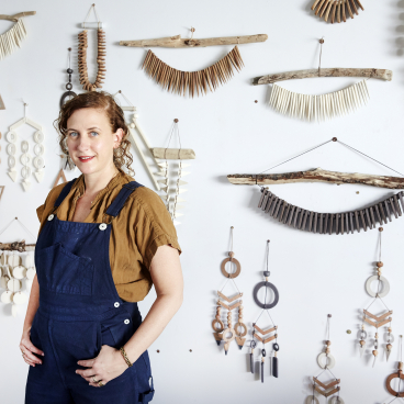 Heather Levine poses in her studio surrounded by unique vintage stoneware wall hangings and clay creations.