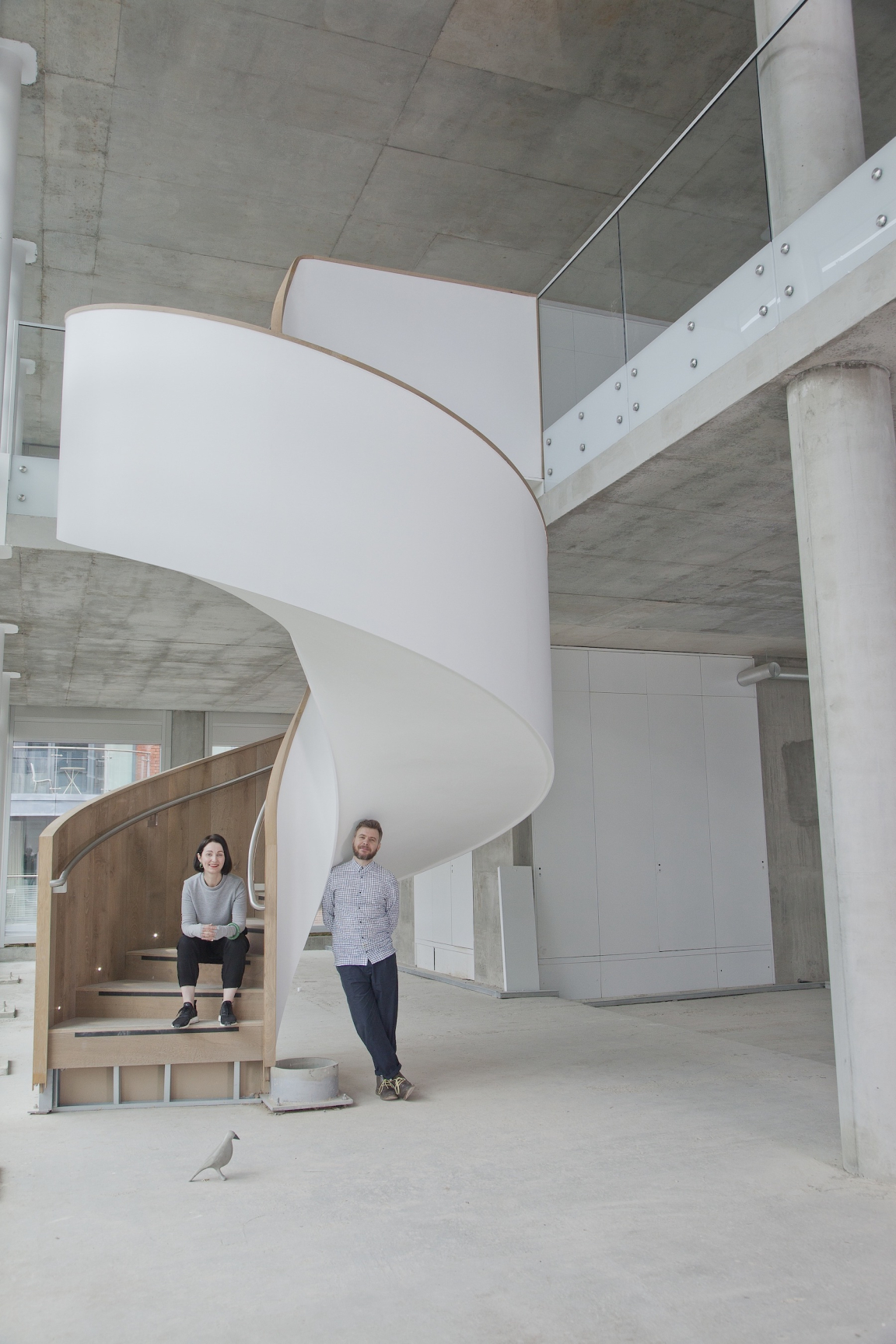 Two creatives pose beside a modern spiral staircase in an unfinished building, showcasing innovative design in North West England.