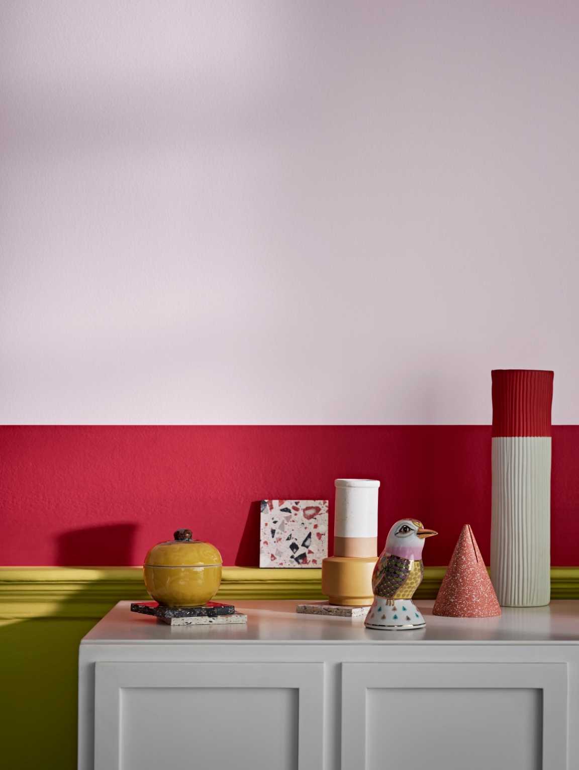 Vibrant color palette featuring decorative objects on a white cabinet against a pink and red wall for autumn inspiration.