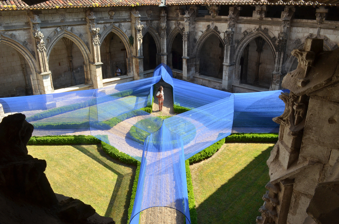 Art installation featuring blue fabric draping over a landscaped courtyard in a historic architectural setting.