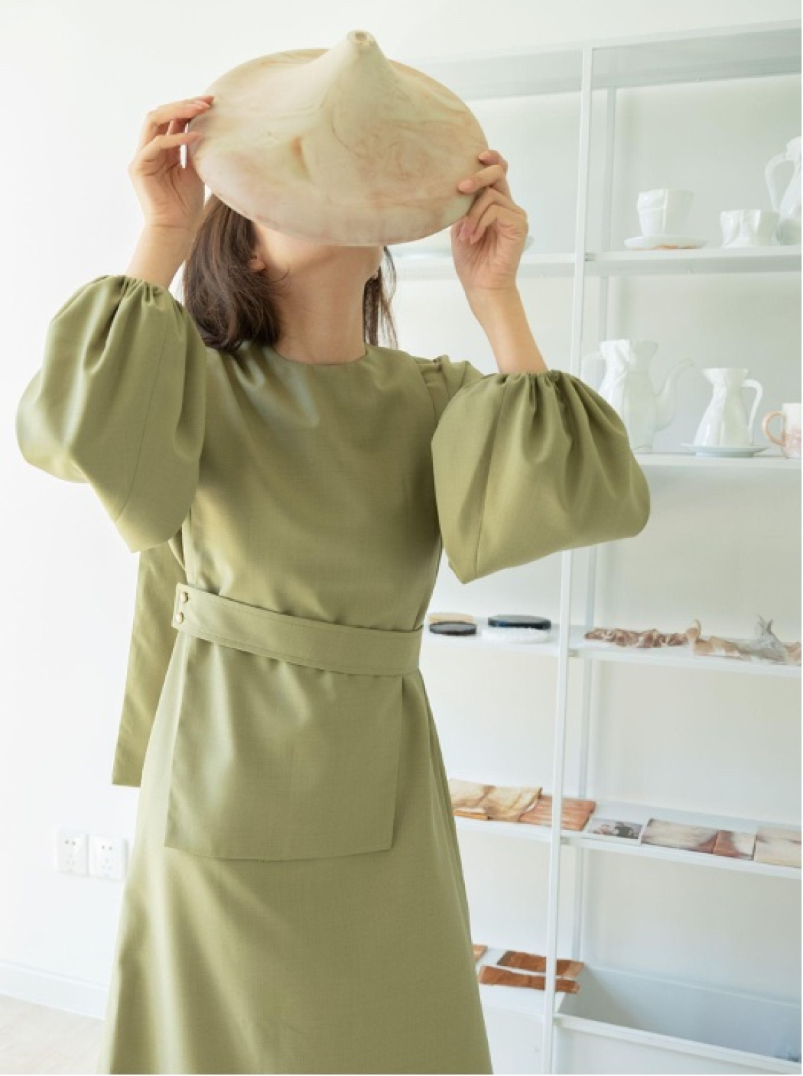 Designer showcasing a unique coffee waste piece while wearing a stylish, sustainable outfit in a bright studio.