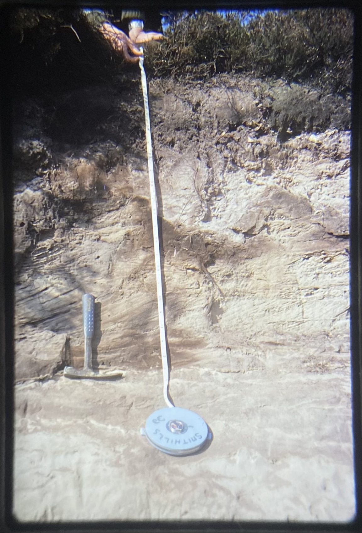 The Tape Measure (1963): An image from 1963 from Georgie’s Grandfather's photo archive: a geology field trip to Dorset, featuring a tape measure and pickaxe, measuring earth layers. Shot on film.