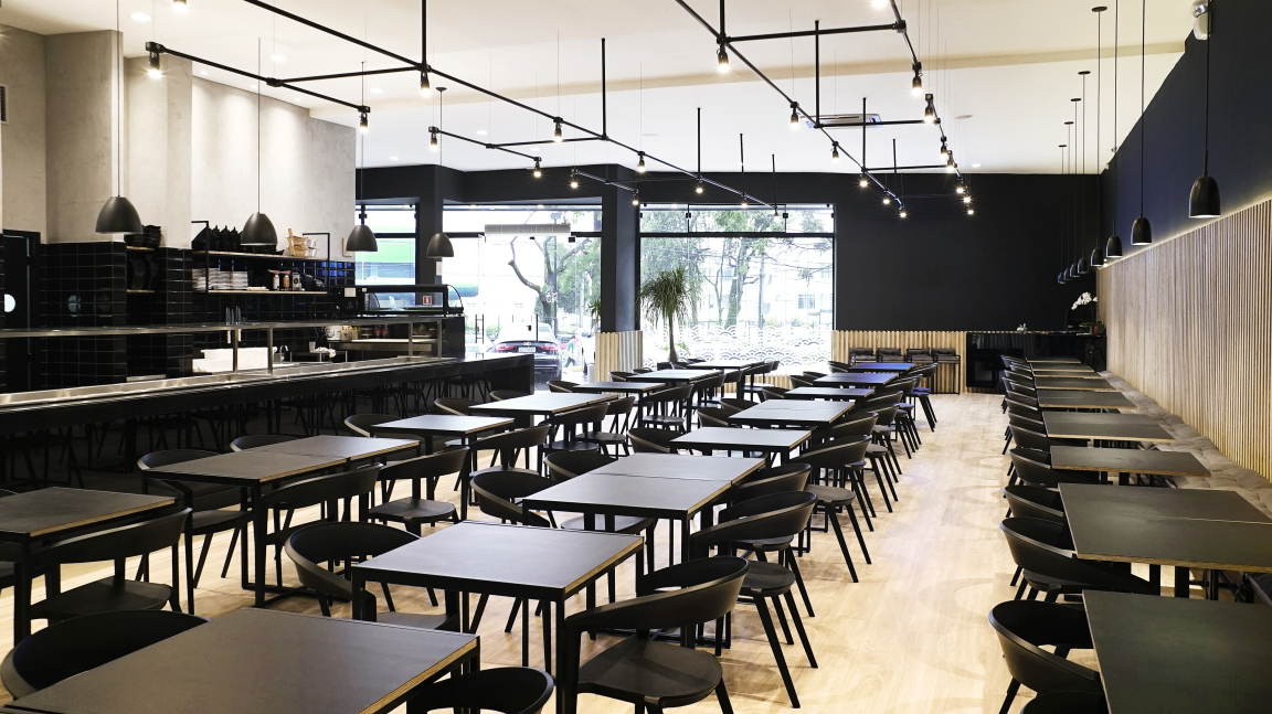 Contemporary interior of Maru Asian Cuisine in Curitiba featuring elegant black tables, wooden accents, and large windows.