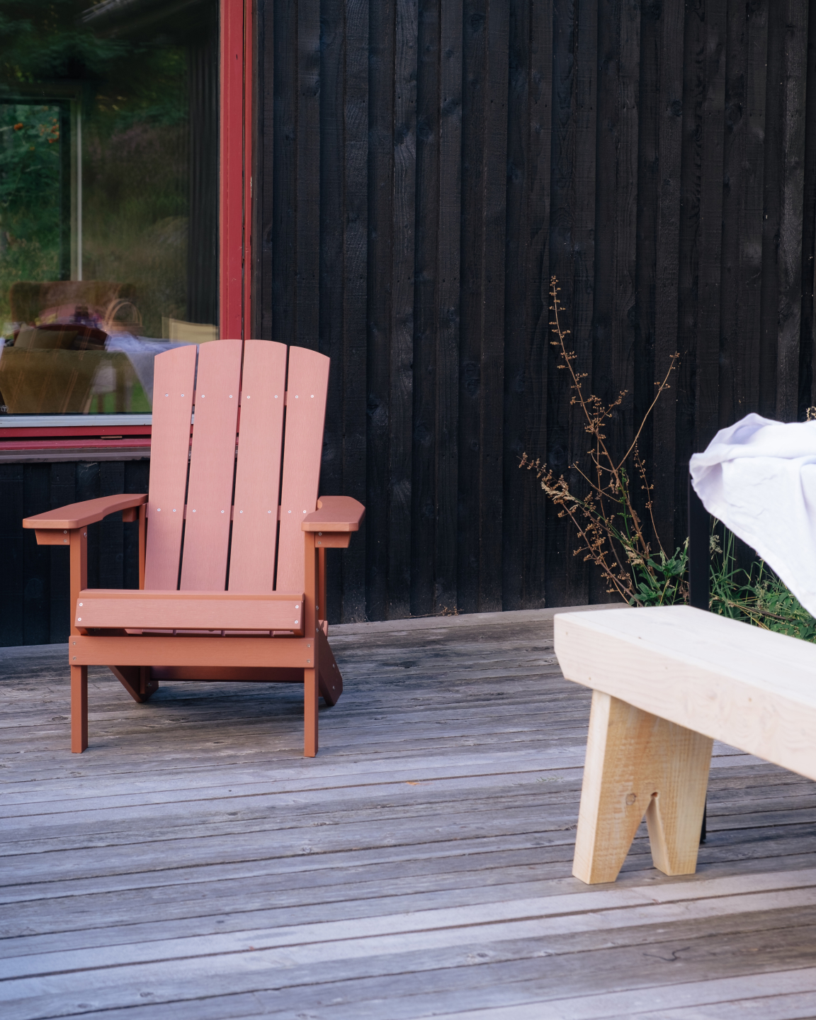 Vibrant red Adirondack chair on a wooden deck beside a minimalist bench, showcasing Scandinavian design influences.