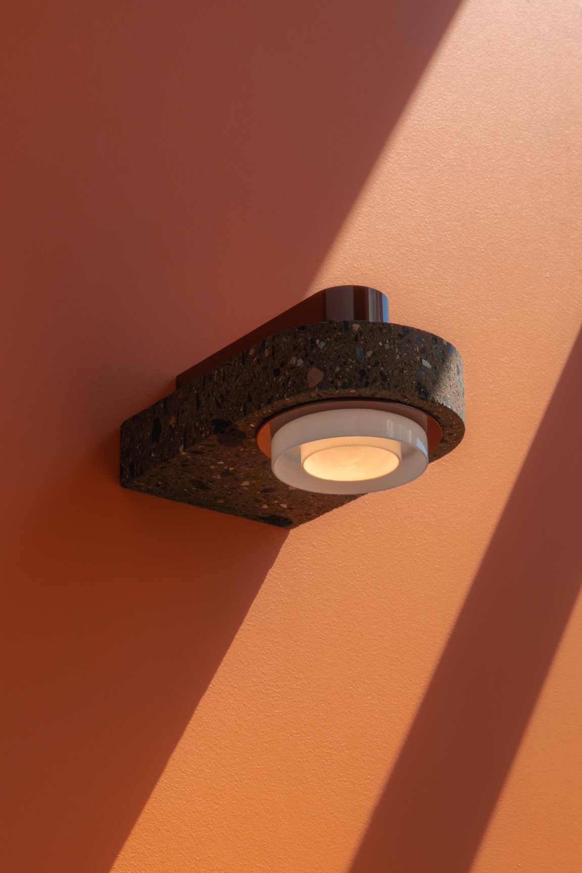 Wall-mounted light fixture featuring volcanic material design, casting gentle shadows on a warm peach wall.