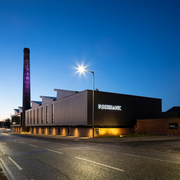 Renovated Rosebank Distillery at dusk, showcasing modern architecture alongside the original historic chimney, blending heritage and innovation.