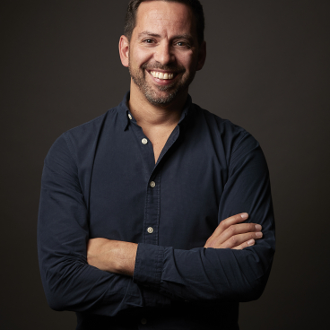 Smiling man in a dark shirt posing confidently, promoting Nulty's online masterclass series for interior designers.