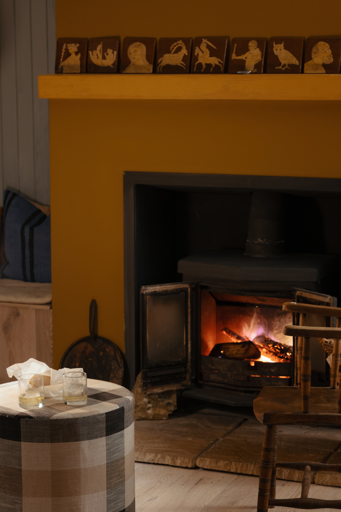 Cozy interior featuring a wood-burning stove, traditional plaid ottoman, and decorative tiles inspired by Scandinavian design.