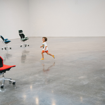 A child runs playfully among Humanscale's Freedom chairs in a spacious, minimalist exhibition space.