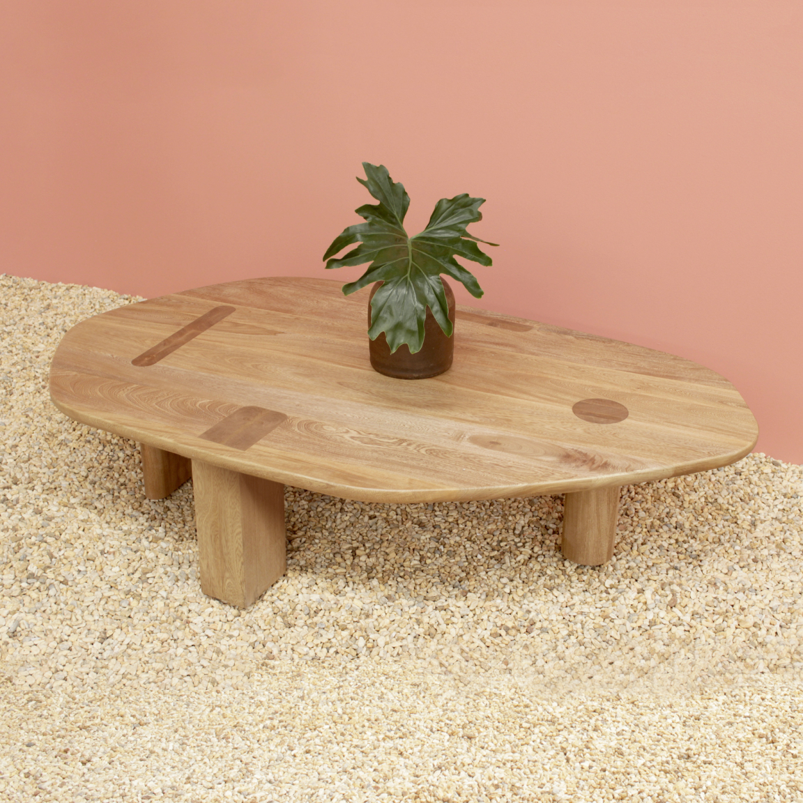 Sleek wooden coffee table with unique design, topped with a green plant, set against a pink background.