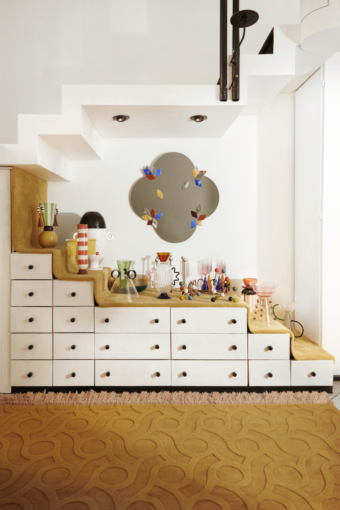 Vibrant display of decorative items and glassware on a stylish staircase cabinet by Serena Confalonieri, showcasing modern design.