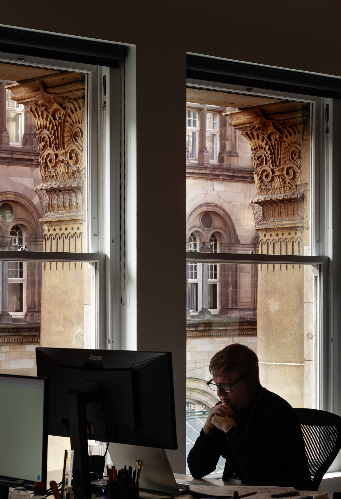 Workplace scene at BDP Glasgow, showcasing historic architecture through large windows and a thoughtful professional at a desk.