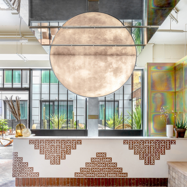 Sleek hotel reception design featuring a large moonlight installation, lush greenery, and sustainable architectural elements in Bermondsey.