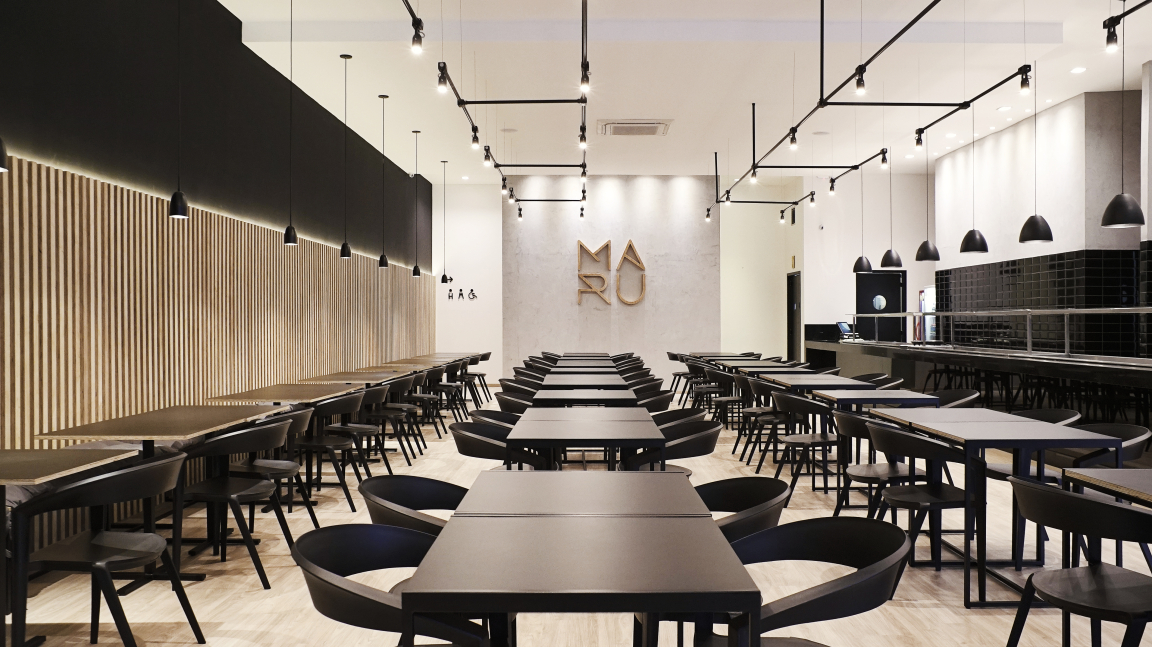 Modern interior of Maru Asian Cuisine in Curitiba, featuring sleek black tables, wooden accents, and stylish pendant lighting.