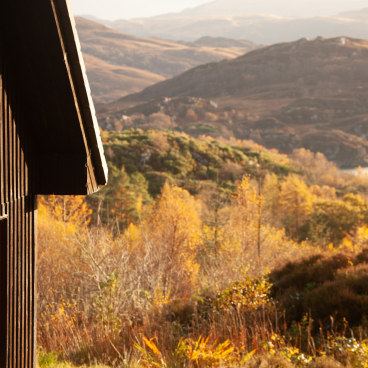 Black timber cabin with large windows nestled in a vibrant autumn landscape, showcasing Hebridean architectural influence.